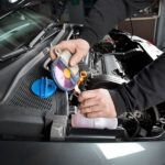 Auto mechanic using tool to check the coolant in a car.