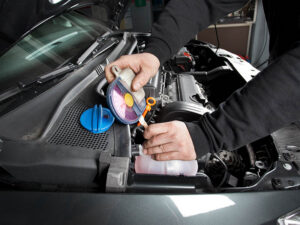 Auto mechanic using tool to check the coolant in a car.